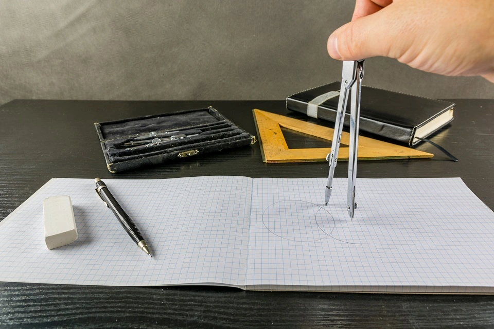 Using a compass on squared paper with maths materials nearby.